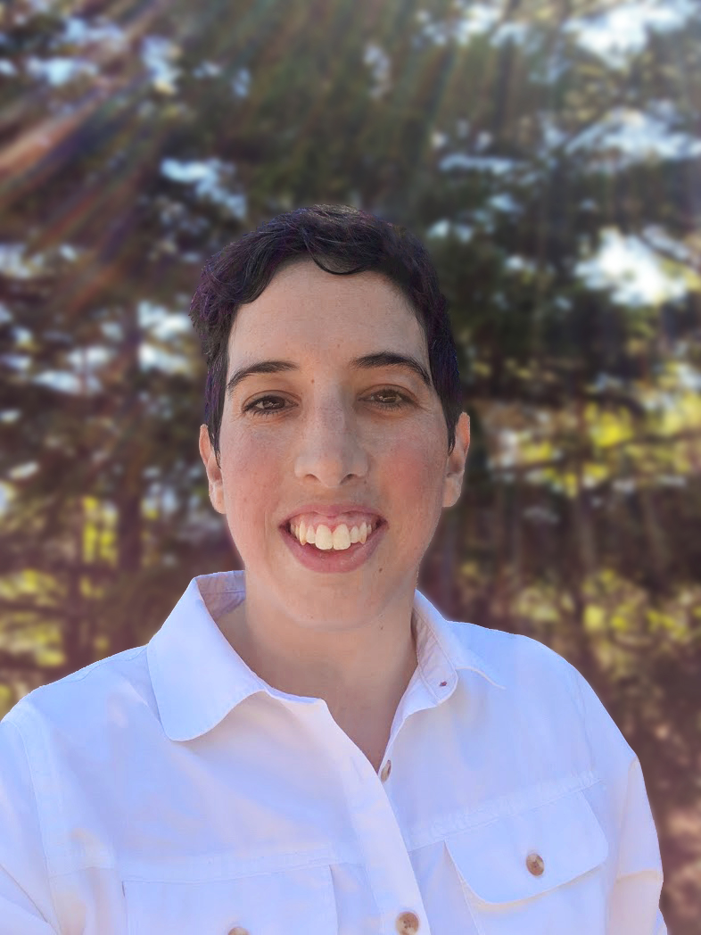 A photo of Katelyn, a white person with short dark hair wearing a white button-up shirt. Smiling at the camera. Outside with trees in the background.